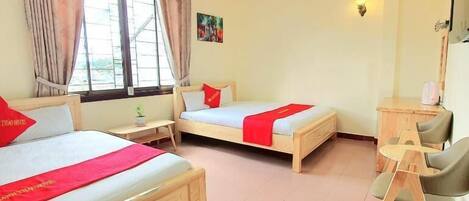 A hotel room with two beds, a desk, a chair, a window with curtains, and a wall-mounted light.