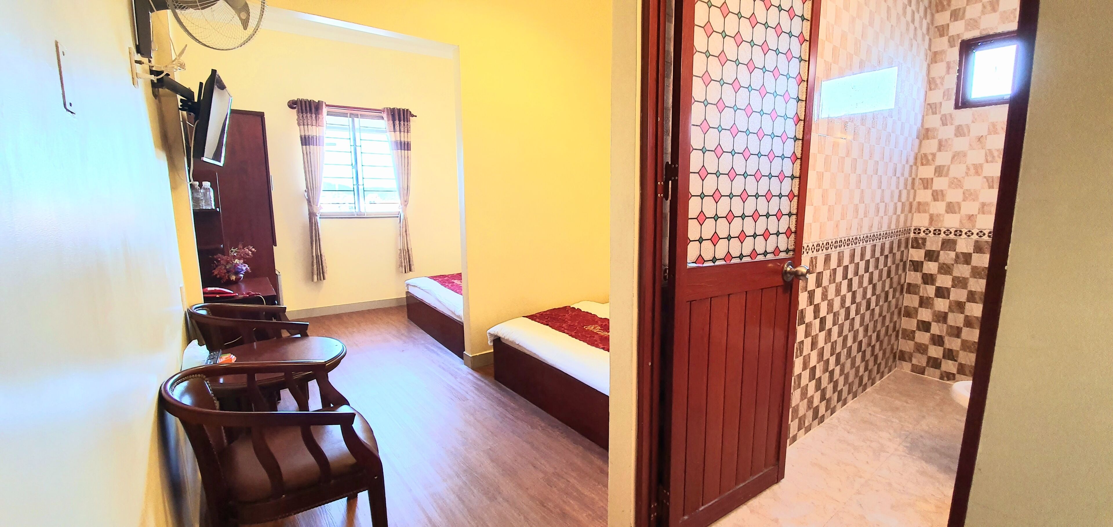 A room with a bed, a desk, a chair, a window with curtains, and a door leading to a bathroom with checkered tiles.
