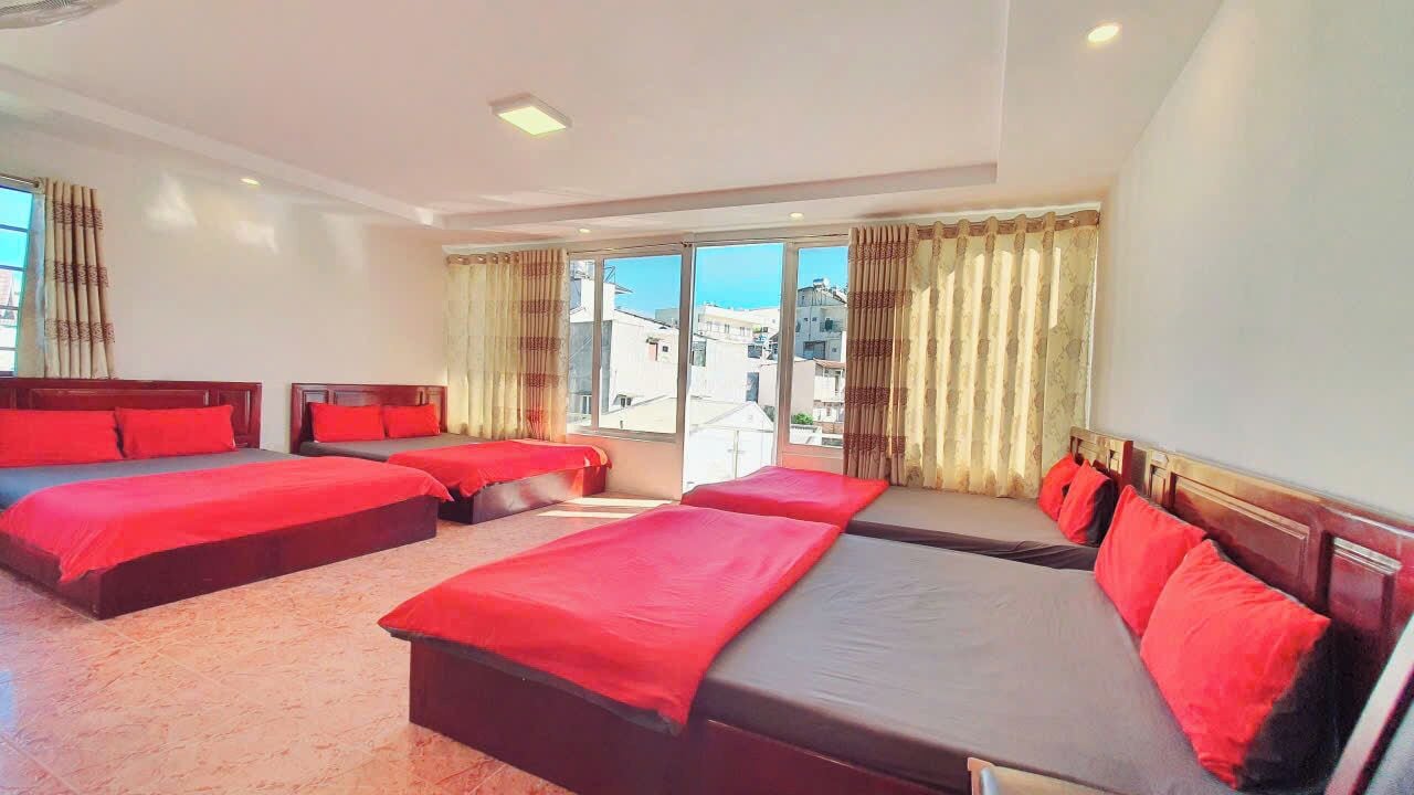 A hotel room with four beds, large windows, and a view of buildings.