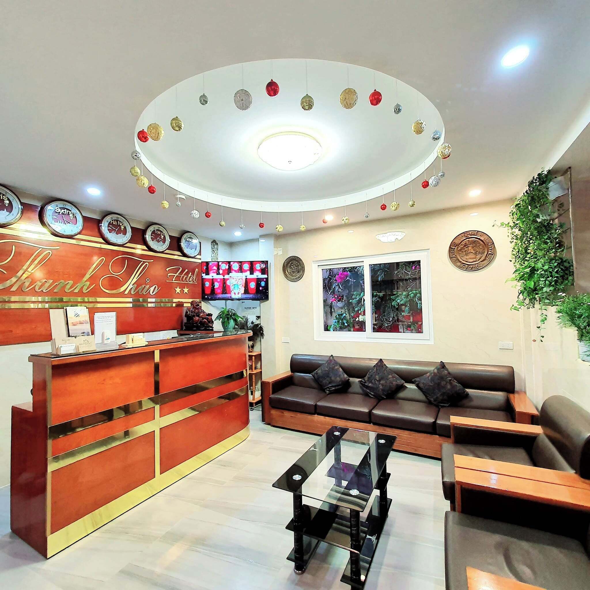 Zona de recepción de hotel con un mostrador de madera, un área de estar con sofá y sillones, un televisor y un techo decorativo.