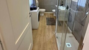 Een kleine badkamer met een douche, toilet en wasmachine.
