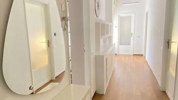 A hallway with a wooden floor, white walls, and a large mirror on a white dresser.