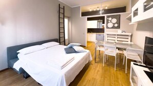 A modern bedroom with a bed, bedside table, and a desk area with chairs and a television.