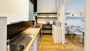 A modern kitchen with a gas stove, oven, and microwave, a dining area with a table and chairs, and a view through a glass door.