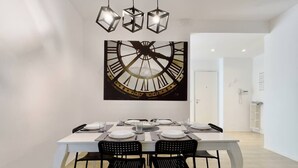Un comedor con una mesa blanca, sillas negras y un mural grande con un reloj en la pared.