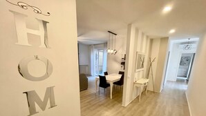 Un pasillo con un letrero que dice 'HOME', un comedor con mesa y sillas blancas, y una lámpara moderna.