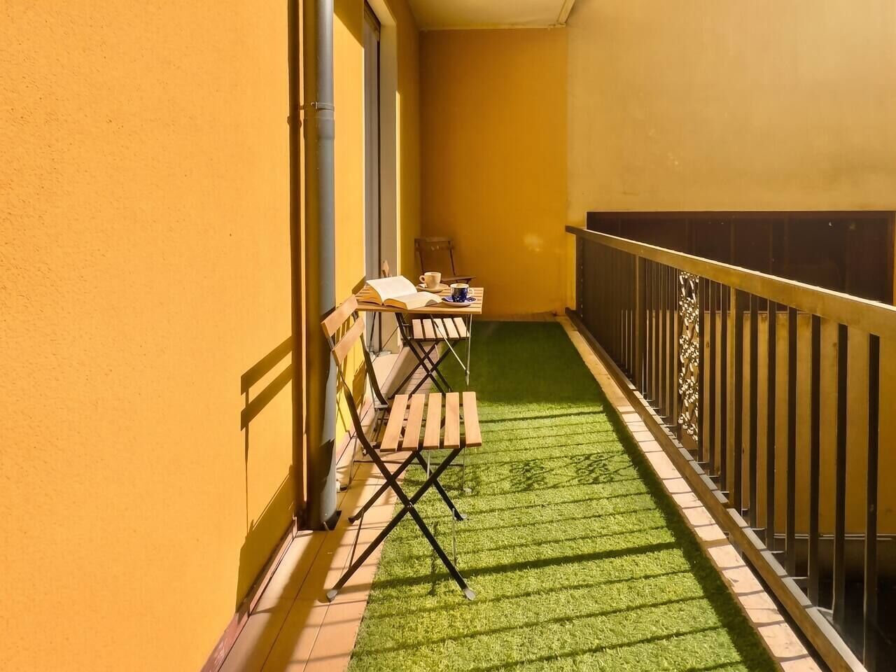 Un balcon avec un revêtement de sol en gazon synthétique, une chaise en bois, une table et une rambarde.
