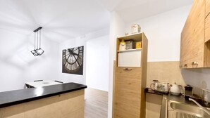 Una cocina compacta con encimera negra, armarios de madera, una lámpara colgante y un reloj en la pared.