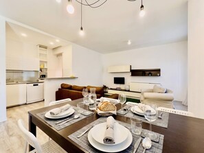 A modern dining area with a dark wooden table set for four, white plates, cutlery, and glasses. A loaf of bread and a bottle of water are on the table. - Leonardo Academy Hub: Comfort and Space in the Center (Sesto Calende)