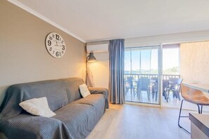 Ein Zimmer mit einer Couch, einer Lampe, einer Uhr und einem Balkon mit Stühlen.