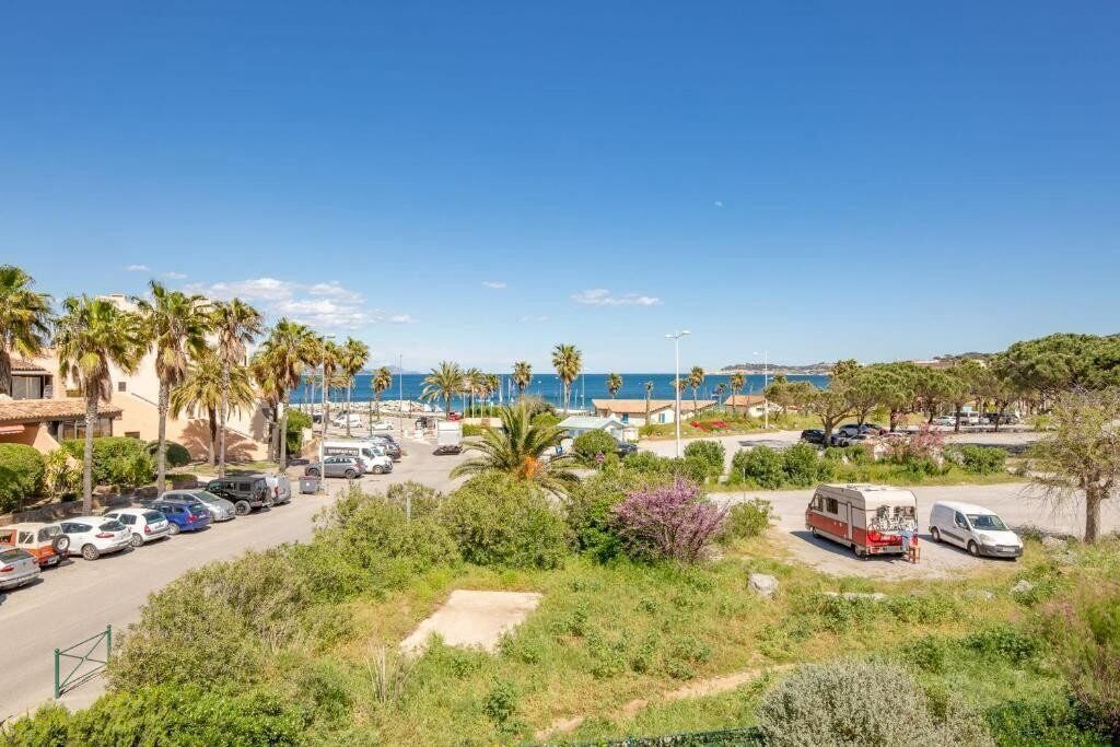 Een parkeerplaats aan de kust met auto's, een caravan en een witte bus.