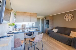 Eine moderne Küche mit Holzsäulen, einem Essbereich mit zwei Stühlen, einem Sofa und einer Wanduhr.