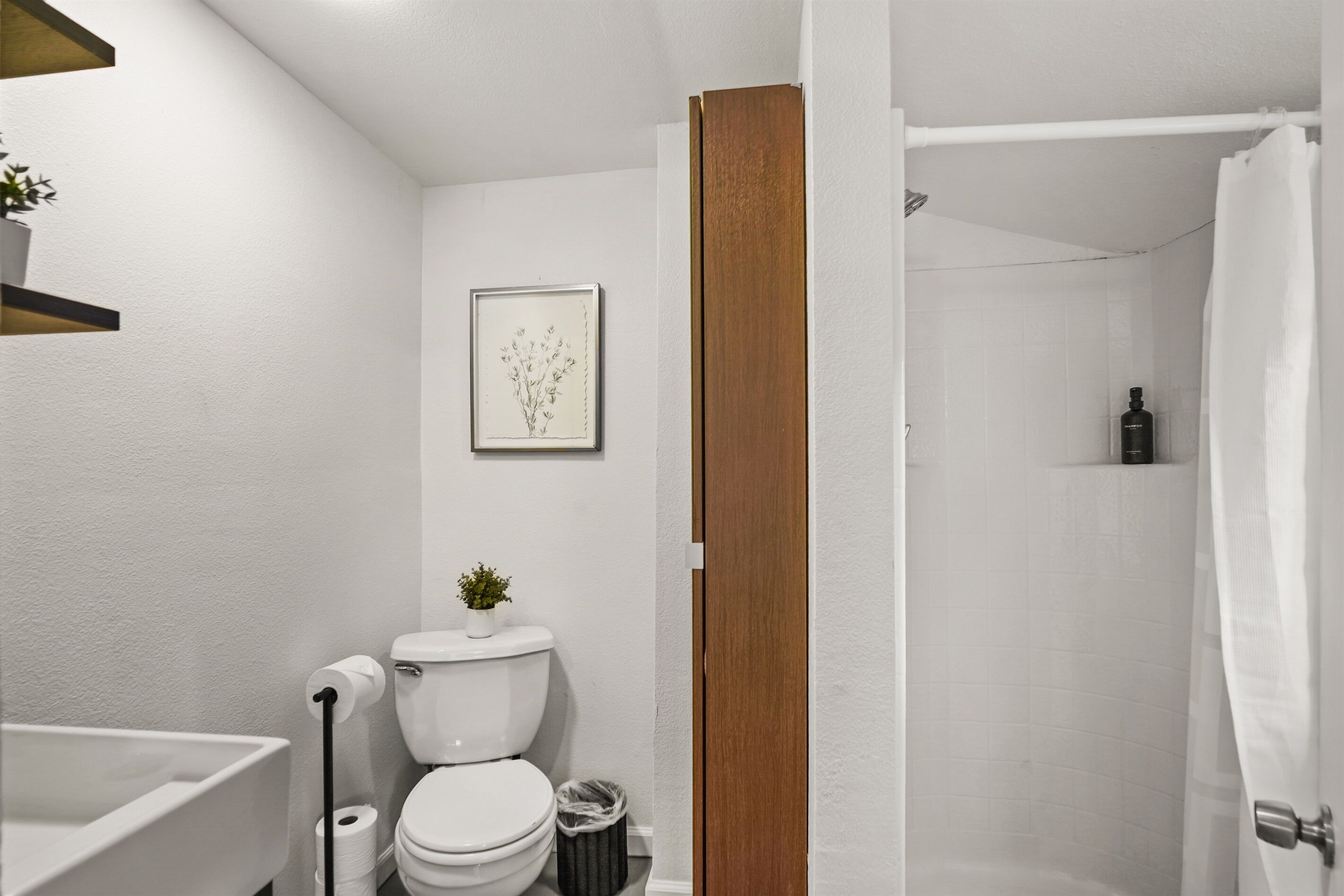 Casa de banho com sanita, lavatório, chuveiro e um quadro emoldurado na parede.