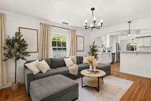 Ein modernes Wohnzimmer mit einem grauen Ecksofa, einem runden Couchtisch und einer Chandelier.