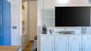 Una habitación con televisión instalada en la pared, cafetera y un mueble con cajones.