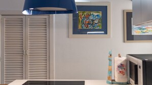 Una habitación con puerta cerrada, una lámpara colgante azul, un cuadro abstracto enmarco, un microondas y un jarrón decorativo.