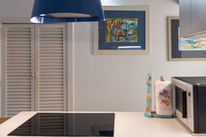 Ein Zimmer mit geschlossener Tür, einer blauen Pendelleuchte, einem gerahmten abstrakten Gemälde, einer Mikrowelle und einer dekorativen Vase.