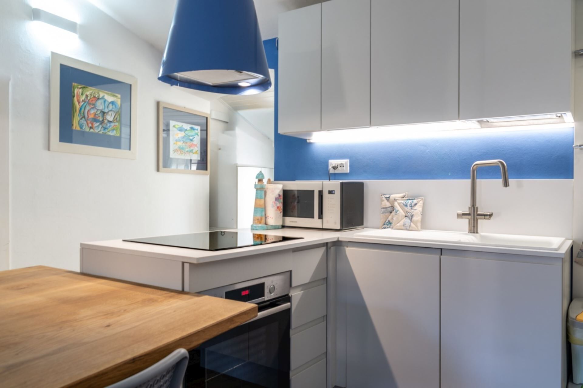 Eine kompakte Küche mit Mikrowelle, Backofen und Spüle, mit einer blauen Akzentwand und modernen Geräten.