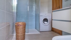 Un baño con cabina de ducha de vidrio, lavadora y cesta de mimbre.