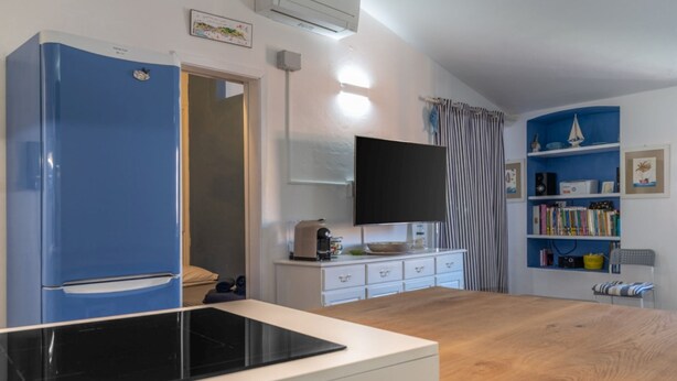 Una cocina compacta con un refrigerador azul, una cocina por inducción negra, una encimera blanca y una mesa de comedor de madera.