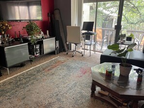 Une pièce dotée d’une grande télévision, d’un bureau, d’une chaise, d’un canapé et d’un balcon agrémenté de plantes.