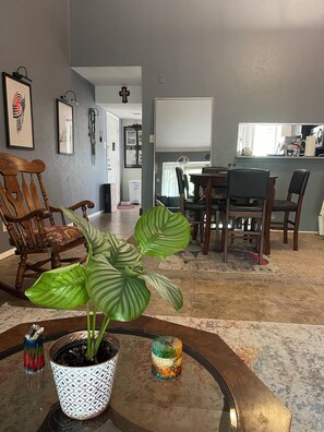 Un salon avec un coin repas, une plante en pot et une cuisine en arrière-plan.