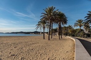 A sandy beach with palm trees and a clear sky. - Location d'un studio cabine pour 4 personnes face mer, centre ville. (LE LAVANDOU)