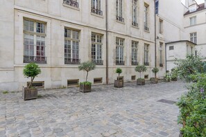 Ein Innenhof mit Steinpflaster, ein Gebäude mit zahlreichen Fenstern und Balkonen sowie Kübelbepflanzung.
