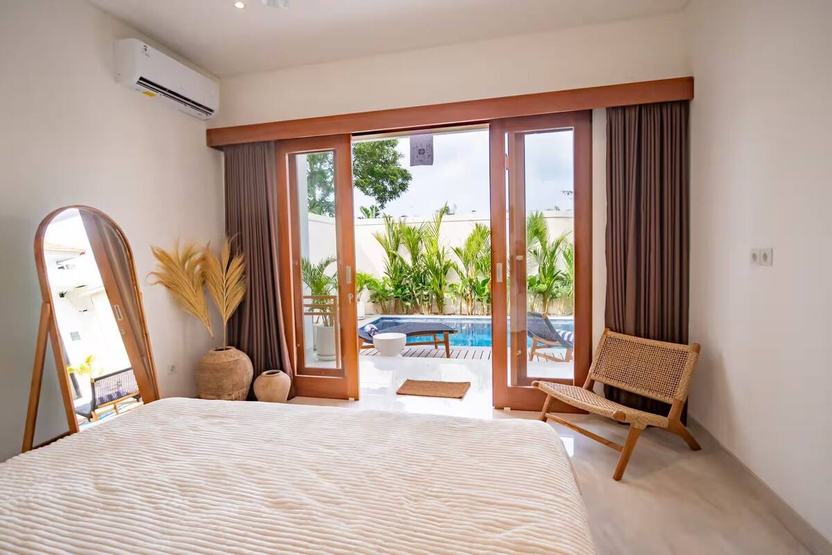 Un dormitorio con una cama grande, una silla, vista a una piscina y una puerta corrediza de vidrio.