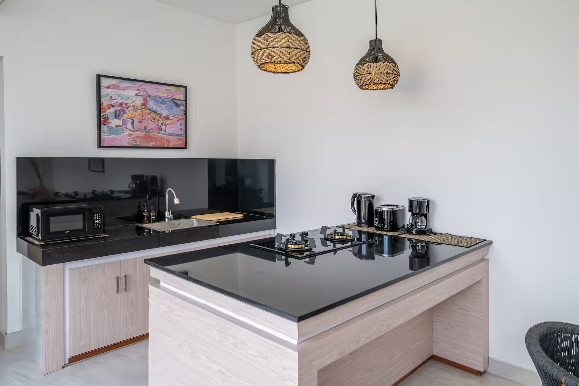 A modern kitchen with a central island, black appliances, and wicker pendant lights.