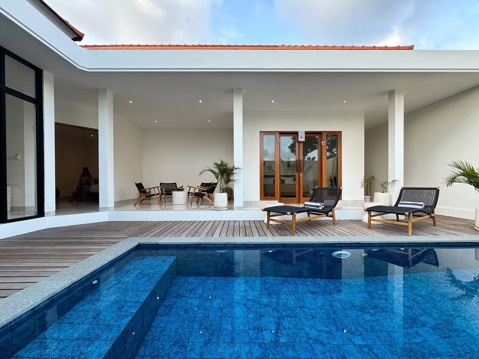 A modern outdoor pool area with a wooden deck, lounge chairs, and a glass-enclosed patio.