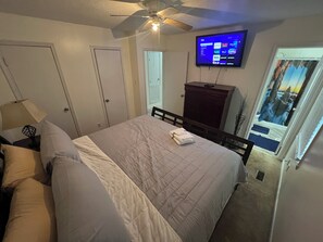 Ein Schlafzimmer mit einem Bett, einem Deckenventilator, einem an der Wand montierten Fernseher und einem Fenster mit Blick.