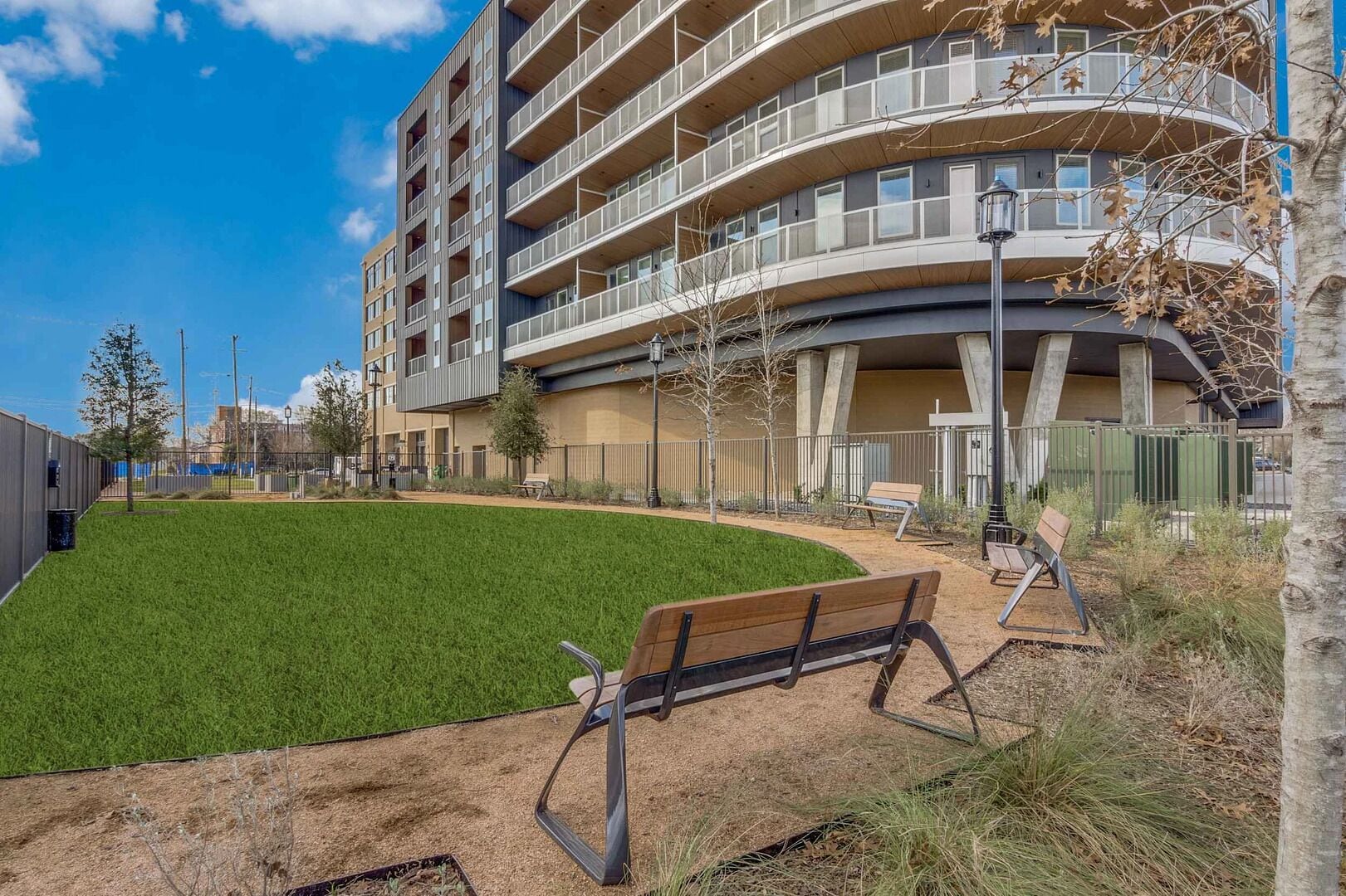 Un bâtiment moderne à plusieurs étages, doté d’une façade incurvée, d’une cour verdoyante et d’un banc.