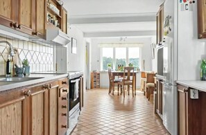A kitchen with wooden cabinets, a tiled floor, a dining area with chairs, and a view through a window. - Nice holiday home in popular Österlen in Skåne! (Tomelilla)