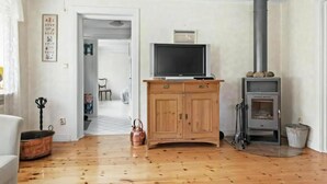 Una sala de estar con piso de madera, un televisor sobre un mueble de madera, una chimenea y una puerta que da a otra habitación.
