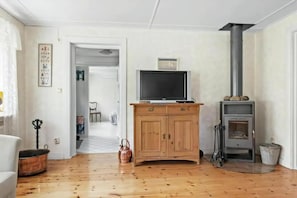 A living room with a wooden floor, a television on a wooden cabinet, a fireplace, and a door leading to another room. - Nice holiday home in popular Österlen in Skåne! (Tomelilla)