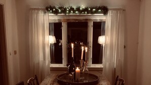 Comedor con mesa de madera, sillas, una alfombra roja, velas y una ventana con cortinas.