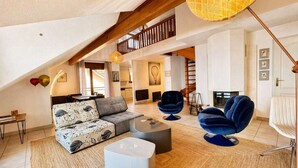 Ein Loft-Wohnzimmer mit einer Couch, einem Hocker und zwei Sesseln, einer Treppe und einem Kamin.