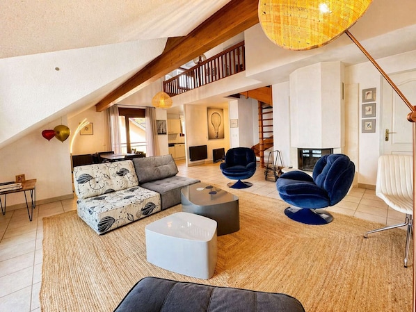 A loft-style living room with a sofa, ottoman, and two chairs, a staircase, and a fireplace. - Exceptional duplex with lake view and direct access to Lake Geneva – Between Évian and Thonon (PUBLIER)