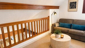 Ein Wohnzimmer mit Holzbalken, einem braunen Sofa, einem runden Couchtisch mit Pflanze und Kerze sowie einer Stehlampe.
