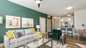 A living room with a sofa, coffee table, and a dining area with chairs and a table. - Landing Furnished Apartments - Midlothian (Midlothian)