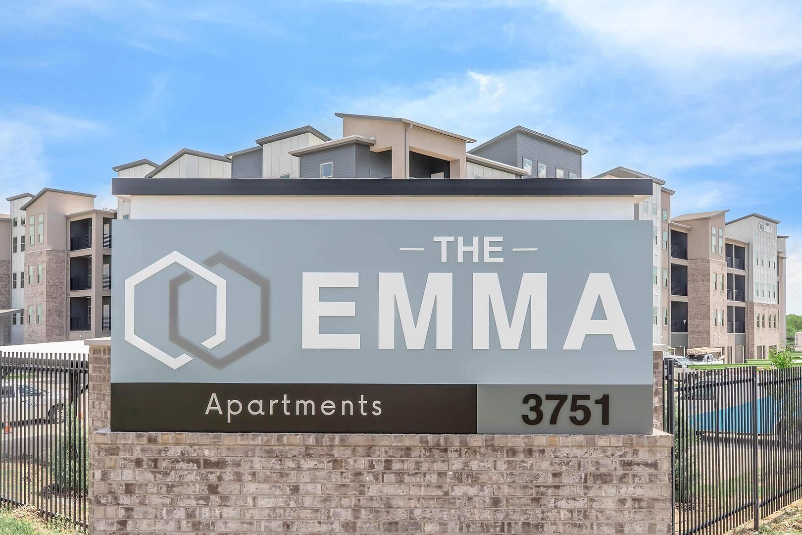 A sign for 'The Emma Apartments' with a hexagonal logo, indicating a residential complex.