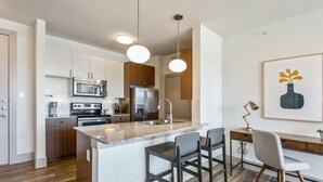 A modern kitchen with a central island, bar stools, a dining area with a table and chairs, and a microwave. - Landing Furnished Apartments - Midlothian (Midlothian)