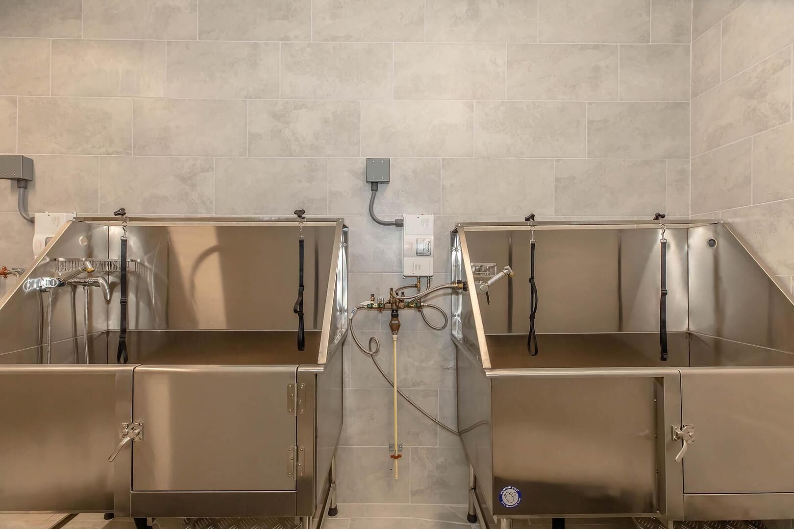 Un baño con dos lavamanos de acero inoxidable, cada uno con un grifo y una manguera, y un enchufe en la pared.