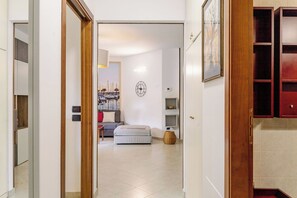 A hallway leading to a bedroom with a bed, a wall clock, and a framed picture.