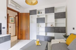 A modern living room with a grey sofa, a coffee table, and a built-in shelving unit with books and decorative items.