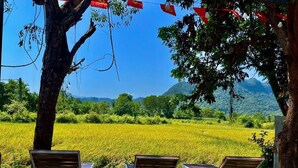 Three sun loungers with open backs facing a lush green field and mountains in the distance. - Retreat Bungalow (Phong Nha)