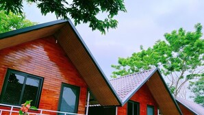A row of red wooden cabins with white railings and a green fence. - Retreat Bungalow (Phong Nha)