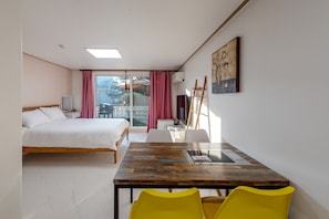 A bedroom with a bed, a desk with chairs, a painting, and a balcony with curtains.