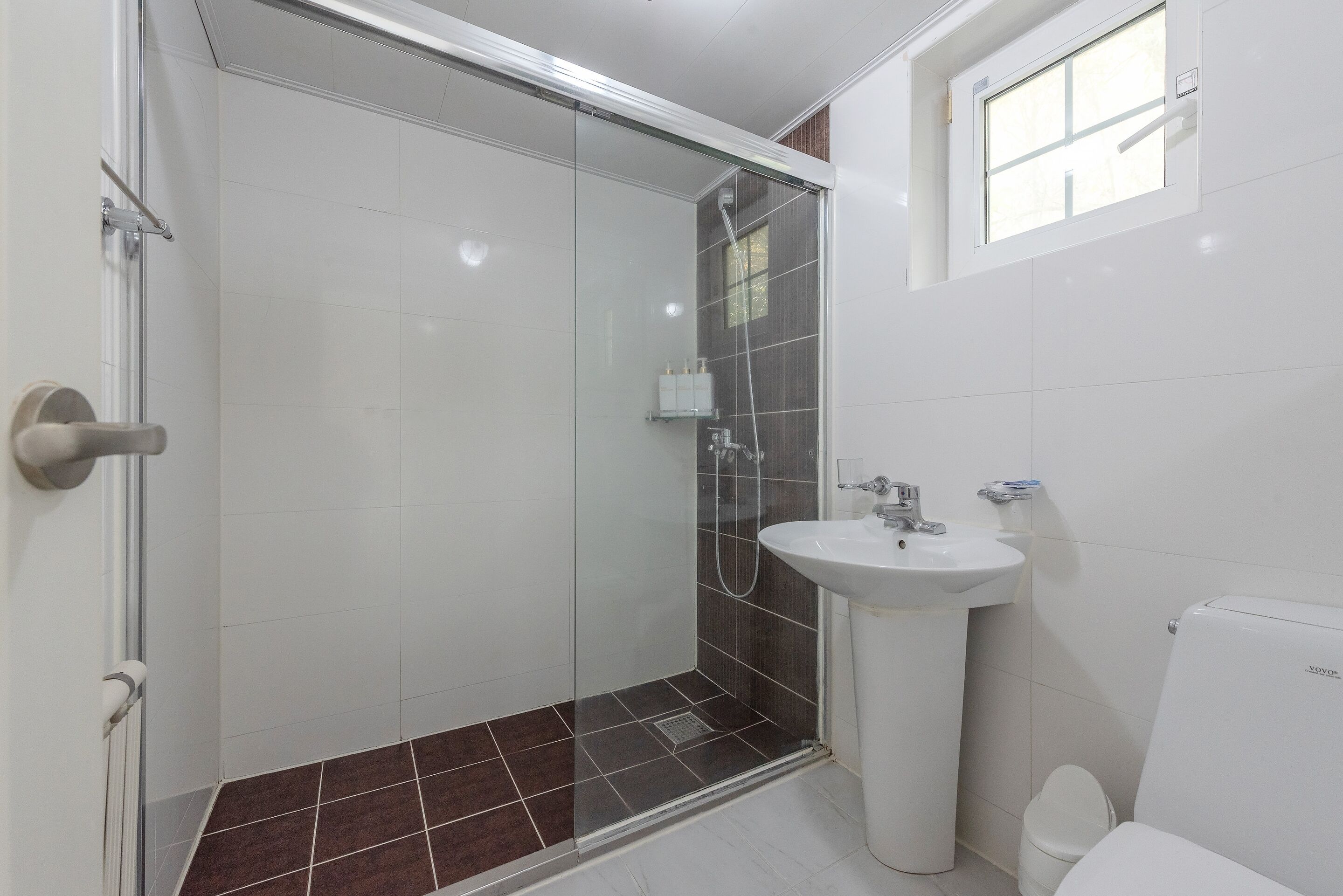Une salle de bain avec une douche à parois de verre, un lavabo sur colonne et des toilettes.